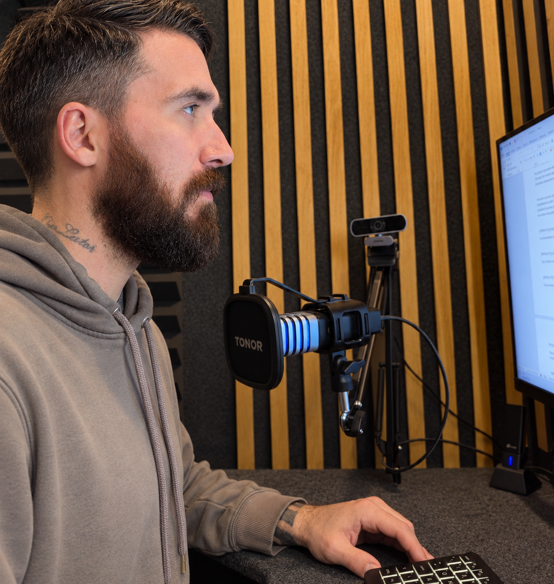 Side-profile portrait at a desk with a microphone and keyboard in a recording studio.